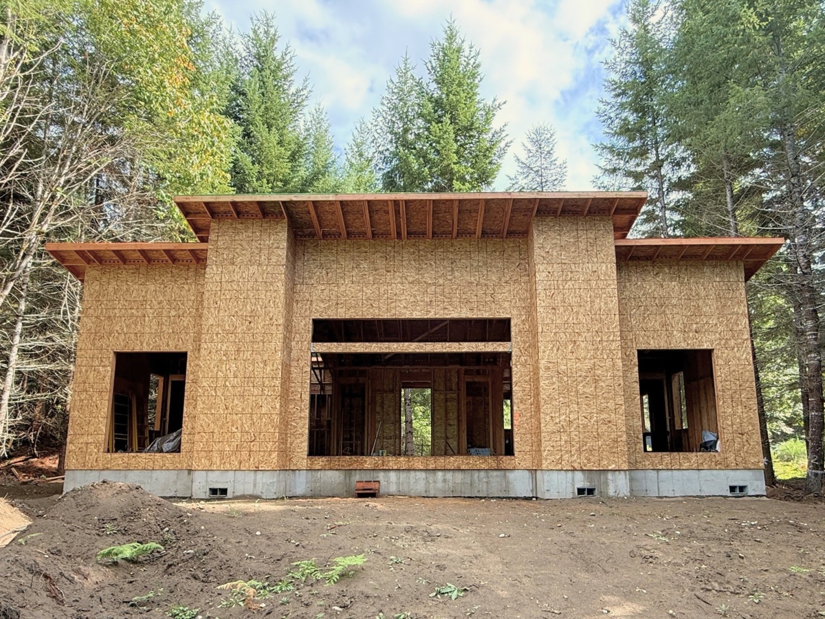 Framing and sheathing complete on the Packwood build, roof structure in place against second-growth forest